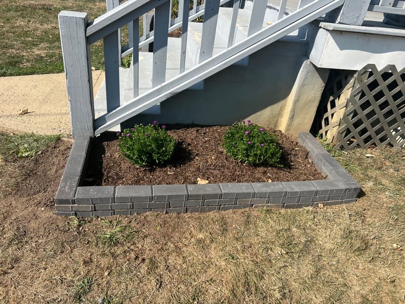 Paver-block edged bed with boxwoods beside deck stairs