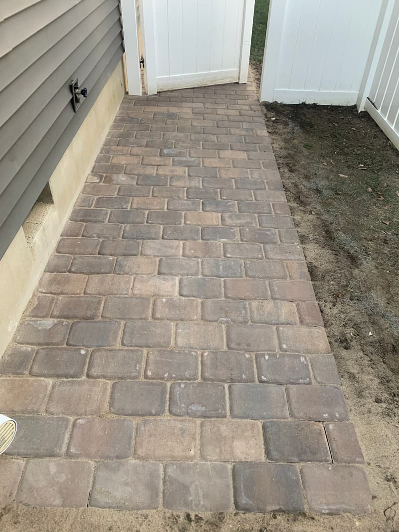 New paver walkway running along the side of a house to a white vinyl gate